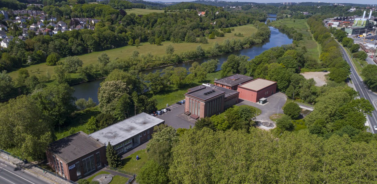 Das Waserwerk Witten im Luftbild. Mehrere große Gebäude neben einem Fluss, umgeben von Bäumen